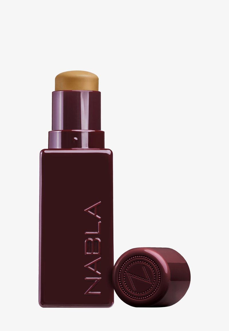 Fond de teint en bâton rouge Bourgogne avec un dessus rond doré. Le flacon présente un logo NABLA en relief et une texture lisse et brillante.
