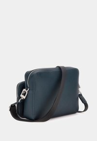 Geantă de umăr din piele de culoare albastru închis, cu accesorii din argint, compartimente cu fermoar dublu și o curea neagră detașabilă, prezentând o suprafață texturată.