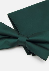Tumma vihreä solmio, joka on valmistettu satiinikankaasta, sillä on sileä pinta ja siihen sopiva taskuliina taitettuna sen viereen, molemmat järjestetty siististi.