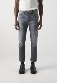 Grå denimjeans med en lätt urtvättad finish, rak skärning och femficksdesign, tillsammans med svarta loafers.