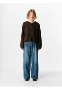 Brun stickad cardigan med knappstängning, två framfickor och långa ärmar, tillsammans med vida blå jeans. Mjuk textur, avslappnad passform.