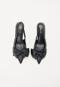 Sorte veganske lær slingback hæle med spidse tæer. Har en stor sløjfe detalje foran og en glat overflade.
