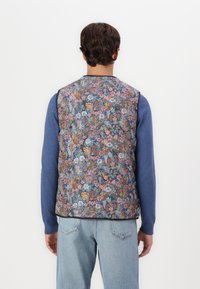Floral-patterned vest with multicolored flowers on a dark background; lightweight fabric; round neckline; paired with a blue long-sleeve shirt.