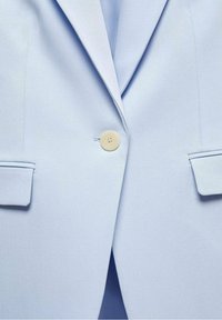 Veste bleu clair avec un seul bouton beige fermé, revers crantés et deux poches à rabat à l'avant.