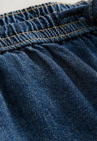 Denim tkanina u plavim nijansama, sa nabranim strukom. Primjetno vidljivo šivanje u kontrastnoj zlatnoj boji. Glatka tekstura.