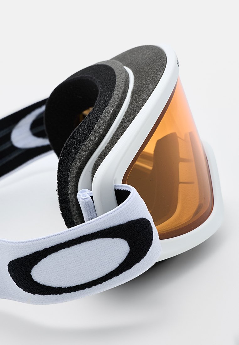 Gafas de esquí con un marco blanco, lente naranja, acolchado de espuma negra y una correa ajustable blanca y negra con un logotipo.