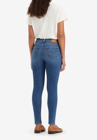 Jeans ajustados de color azul hechos de mezclilla, con un diseño de cintura alta, un parche de cuero en la parte posterior, dos bolsillos traseros y un corte slim en las piernas.