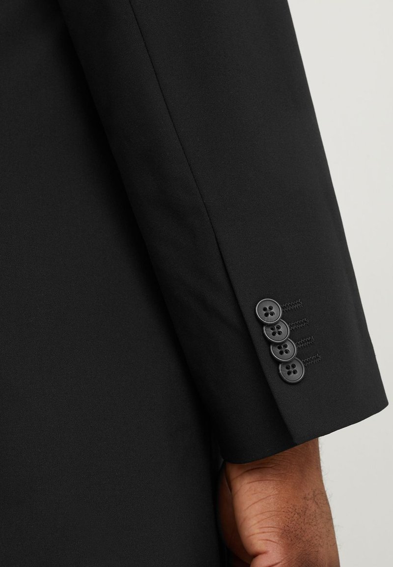 Manga de saco de traje negro a medida con cuatro botones negros, detalles de costura sutiles y textura de tela suave y estructurada.