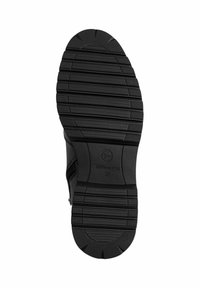 Schwarze Schuhsohle mit einer strukturierten Gummioberfläche, die ein gemustertes Grip-Muster aufweist, und dem eingestempelten Markennamen "Tamaris" in der Nähe der Ferse.