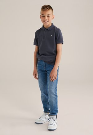 Marineblauwe polo met korte mouwen en een kraag, gecombineerd met lichtblauwe jeans en witte sneakers met donkere accenten.