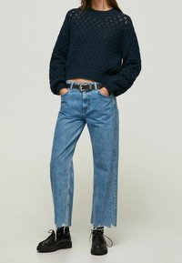 Granatowy krótki sweter dzianinowy z teksturowanym wzorem, zestawiony z jasnoniebieskimi jeansami o wysokim stanie i prostych nogawkach, z surowymi wykończeniami i czarnymi botkami na sznurowadła.