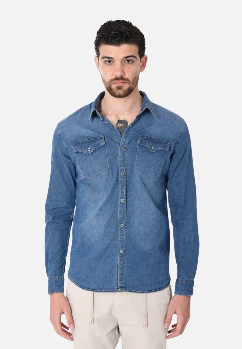 Camicia in denim azzurro chiaro con maniche lunghe, chiusura frontale con bottoni, due tasche sul petto e orlo curvo. Il materiale ha una superficie liscia e texture.