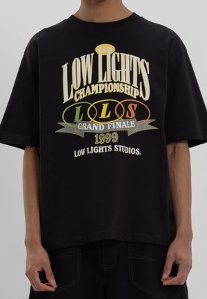 Black cotton t-shirt with oversized fit featuring multicolored graphic text: "LOW LIGHTS CHAMPIONSHIP," "GRAND FINALE," and "1999."