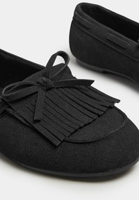 Schwarze Wildleder Slipper mit einem Fransenakzent und einer Schleifendetail auf der Vorderseite. Glatte Textur mit einer runden Zehenform und flexibler Sohle.