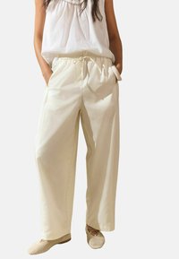 Pantalons larges de couleur crème avec une ceinture élastique et des poches latérales. Assortis à des chaussures à enfiler tissées de couleur beige clair.