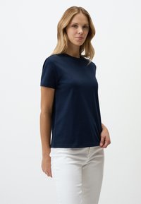 T-shirt blu navy a maniche corte realizzato in morbido cotone. Collo rotondo e design semplice e classico. Indossato con jeans bianchi, caratterizzati da una vestibilità rilassata.