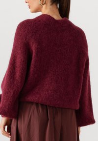 Bordeaux mohair trui met een zachte textuur, brede mouwen en een ronde halslijn, gecombineerd met een bruine geplooide rok.