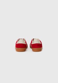 Røde semskede sneakers med en beige krave og hvide detaljer ved hælen, med en gummisål og glat tekstur.