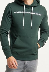 Felpa verde in cotone con testo stampato bianco, coulisse e tasca frontale. Presenta polsini e orlo a coste. Include un'etichetta di marca sul maniche.