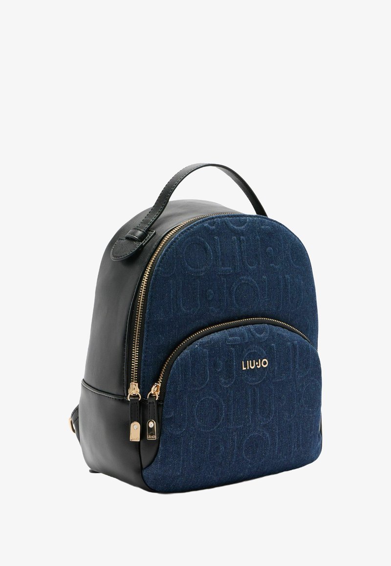 Blauwe suède en zwarte leren rugzak met goudkleurige accenten, ronde vorm, gegraveerd logo en ritsvak aan de voorkant.