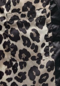 Leopardskin patroon stof in beige en zwart met een klein ritsvakje. Zachte textuur met contrasterende zwarte accenten langs de randen.