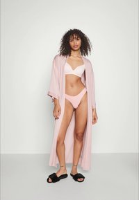 Helle rosa Kimono-artige Robe, weicher Stoff, knielang, getragen über einem weißen BH und hellrosa Panties. Schwarze flauschige Slipper sind enthalten.