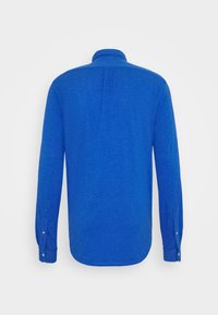 Chemise homme bleue à manches longues vue de dos avec poignets boutonnés et col plié sur un fond uni.