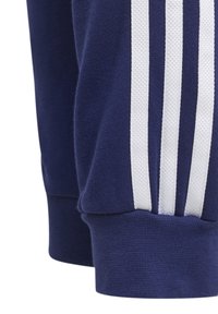 Tummansininen kangas, jossa on kolme pystysuuntaista valkoista raitaa, lähellä kuvattuna ribbikantti ja osa hihaa.