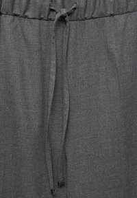 Pantalons avec taille élastique grise et cordon de serrage, fabriqués en tissu texturé. Présentent une finition lisse et un design simple.