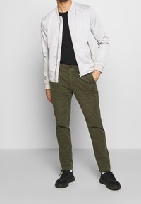 Light gray bomber jacket, black t-shirt, olive green pants, and black sneakers. Smooth fabric with ribbed cuffs and waistband, casual fit.