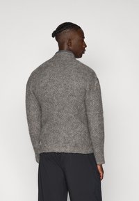 Suéter de punto texturizado gris con cuello alto, mangas largas y un corte relajado. Presenta costuras visibles y un dobladillo sin terminar.