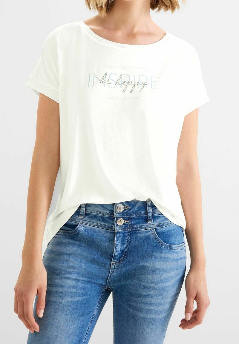 Vit t-shirt med kort ärm och rund halsringning, prydd med ljusblå text och dekorationer, tillsammans med mid-blå denimjeans.