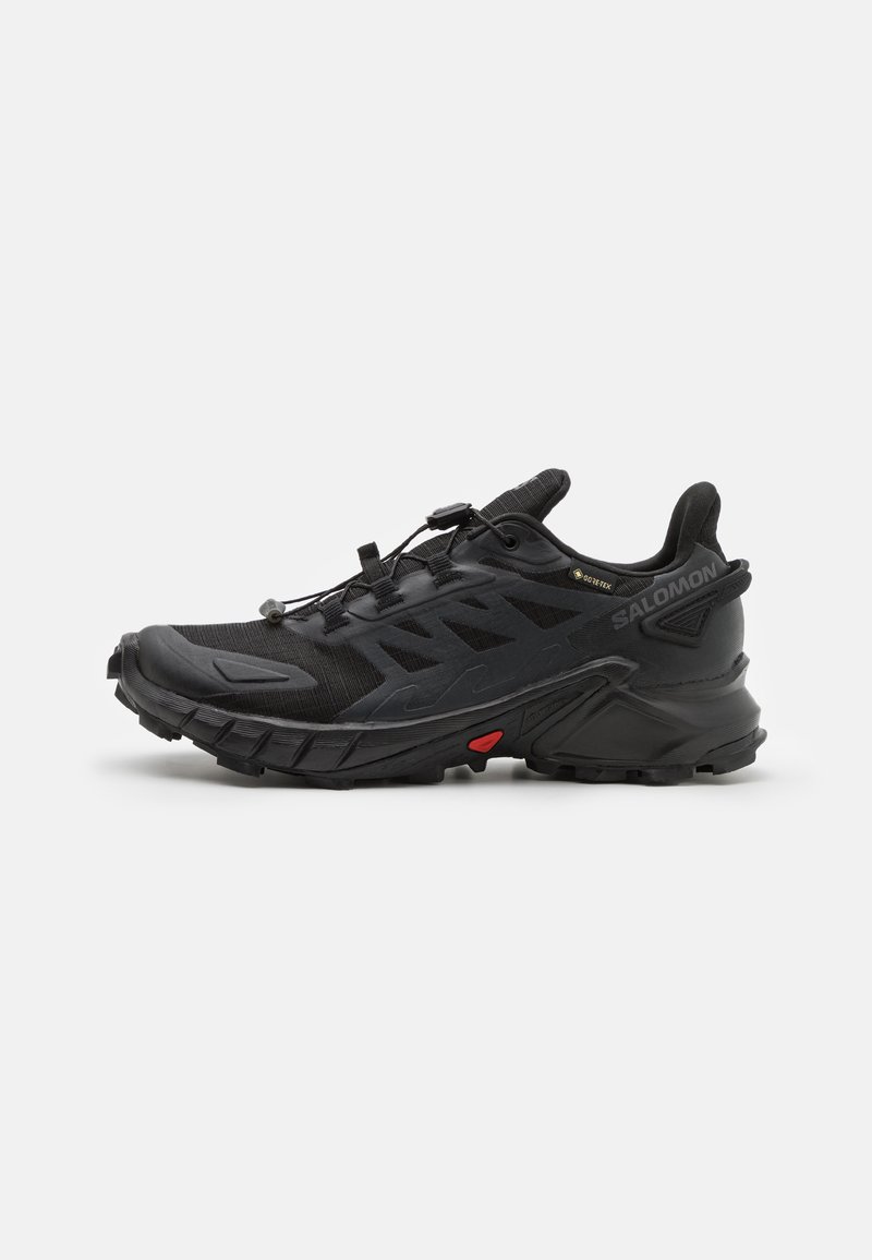Des chaussures de sport noires avec un dessus texturé, dotées d'un système de lacets sécurisé, d'une semelle rembourrée et d'un accent rouge prominent sur le côté.