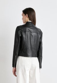 Svart läderjacka med en figursydd design, dragkedjeärmar och svängda sömmar. Baksidan har en slät yta med subtila stygnsdetaljer.