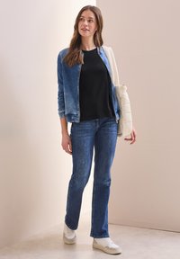 Jeansjacke in Hellblau mit einem verblassten Effekt, schwarzes Oberteil, blaue Jeans, weiße Sneakers und eine cremfarbene Umhängetasche.