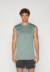 Lys grøn, ærmeløs træningsskjorte med en glat tekstur, rund halsudskæring og sort Nike-logo på brystet. Båret med mørke shorts.