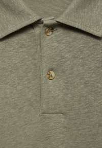Khaki polo tričko s texturovaným pleteným vzorem, špičatým límečkem a jedním knoflíkem se mramorovým povrchem.