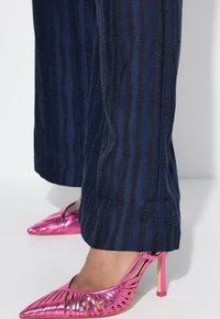 Námořnické kalhoty s vertikálními texturovanými pruhy; spárovány s kovovými růžovými lodičkami na vysokém podpatku, které mají kosočtvercový design a průhledné podpatky.