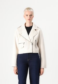Cropped white biker jacket made of soft material, featuring zippered pockets, a notched lapel, and a fitted silhouette. Paired with dark blue jeans.