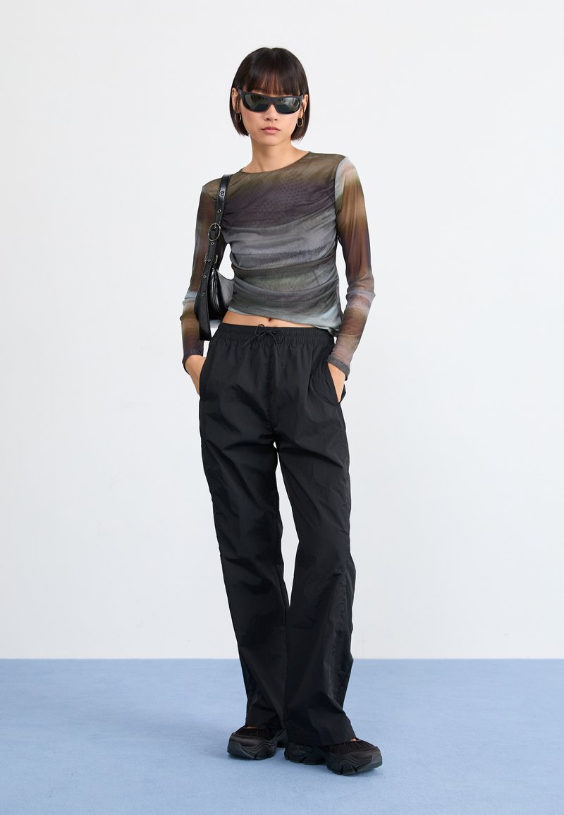 Haut à manches longues en tissu translucide multicolore, présentant des rayures ondulées ; associé à un pantalon noir ample et des chaussures noires en chunky.