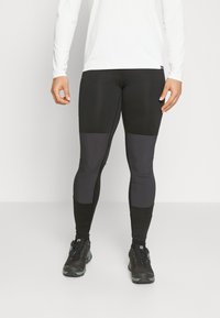 Zwarte sportleggingen met een strakke pasvorm en tinten grijs op de bovenbenen en schenen. Het materiaal lijkt rekbaar en soepel.