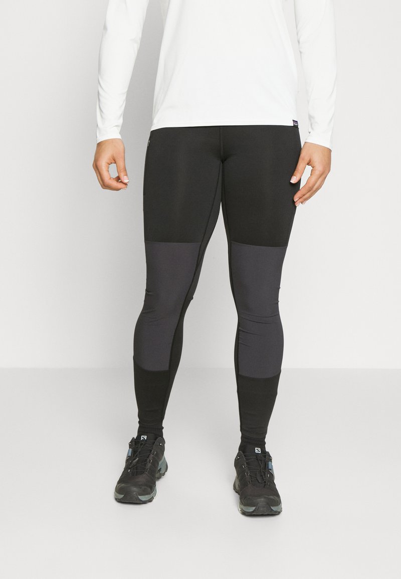 Zwarte sportleggingen met een strakke pasvorm en tinten grijs op de bovenbenen en schenen. Het materiaal lijkt rekbaar en soepel.