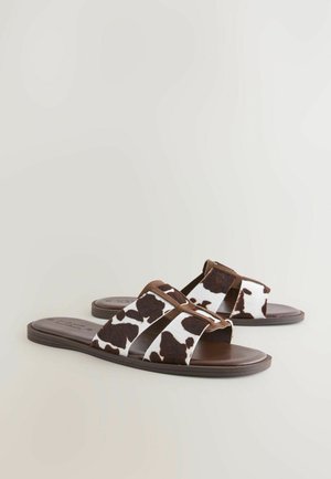 Brown and white cow print slide sandals with two wide straps, a flat brown sole, and soft texture. Suitable for casual wear.