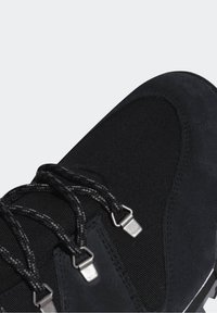 Chaussure de randonnée noire combinant du daim lisse et un tissu texturé, équipée de lacets noirs et d'accentuations métalliques.