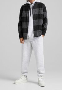 Svart och grå rutig flanellskjorta, lager-på-lager över en grå huvtröja och matchad med grå mjukisbyxor. Vita sneakers kompletterar outfiten.