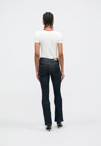 Hvit t-skjorte med korte ermer og rød kant rundt halsen, kombinert med mørkeblå vide jeans med lærmerke og to baklommer.