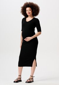 Sort ribbet midi kjole med V-udskæring, korte ærmer og sideslids. Båret med sorte strop sandaler. Blødt, strækbart stof.
