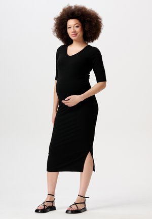 Robe midi noire côtelée avec un col en V, des manches courtes et des fentes sur les côtés. Portée avec des sandales noires à lanières. Tissu doux et extensible.