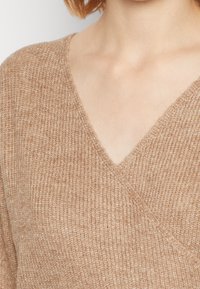Pull en maille de couleur brun clair avec un col en V et un motif texturé. Tissu doux de poids moyen avec une coupe décontractée et des côtes discrètes.