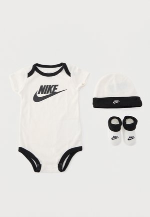 Body bébé Nike blanc et noir, chapeau assorti et chaussettes posés à plat sur un fond blanc.
